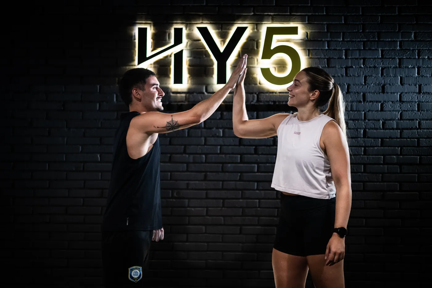 La entrenadora y un alumno chocando la palma bajo el rótulo de neón de HY5.